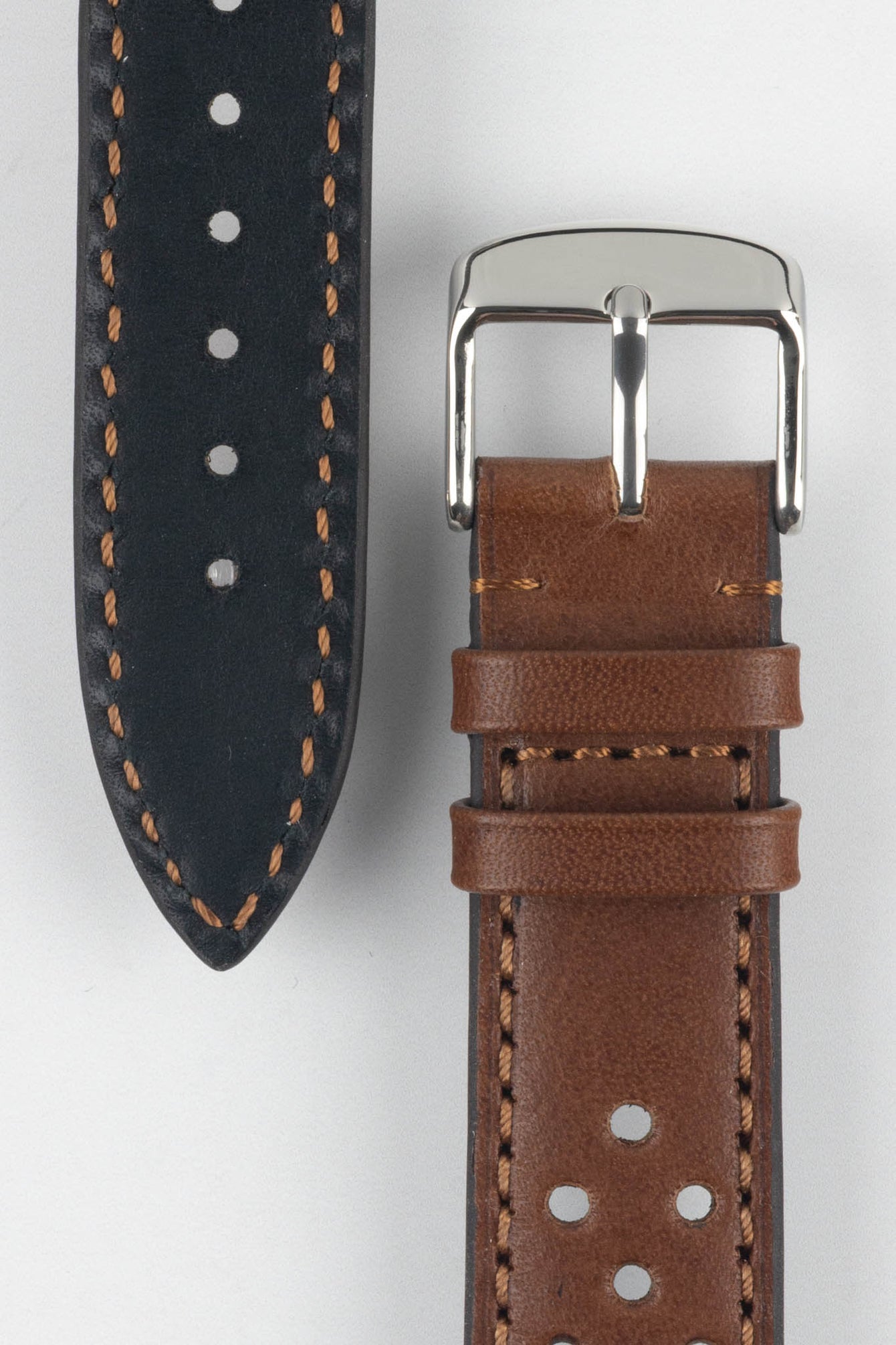 Close-up product shot of a brown perforated leather watch strap paired with a black underside strap segment, both featuring contrast stitching. A polished silver pin buckle is attached to the brown strap, and the components are arranged on a plain light background to highlight the leather texture, perforations, and stitching details.