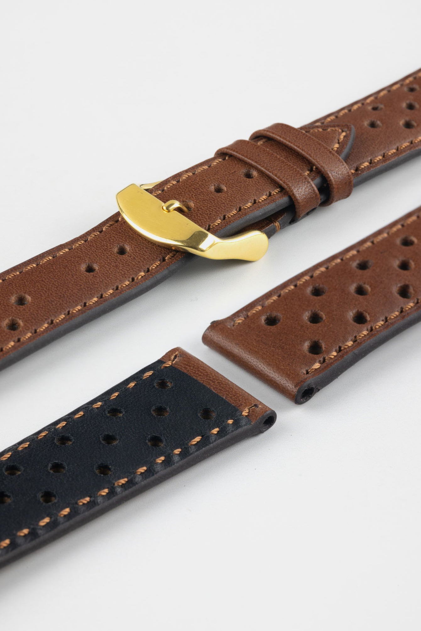 Close-up product shot of brown perforated leather watch strap components with contrast stitching, including one fitted with a polished gold-tone deployment clasp. Additional strap sections, including one with a black underside, are arranged on a plain light background to highlight the leather texture, perforations, and metal hardware details.