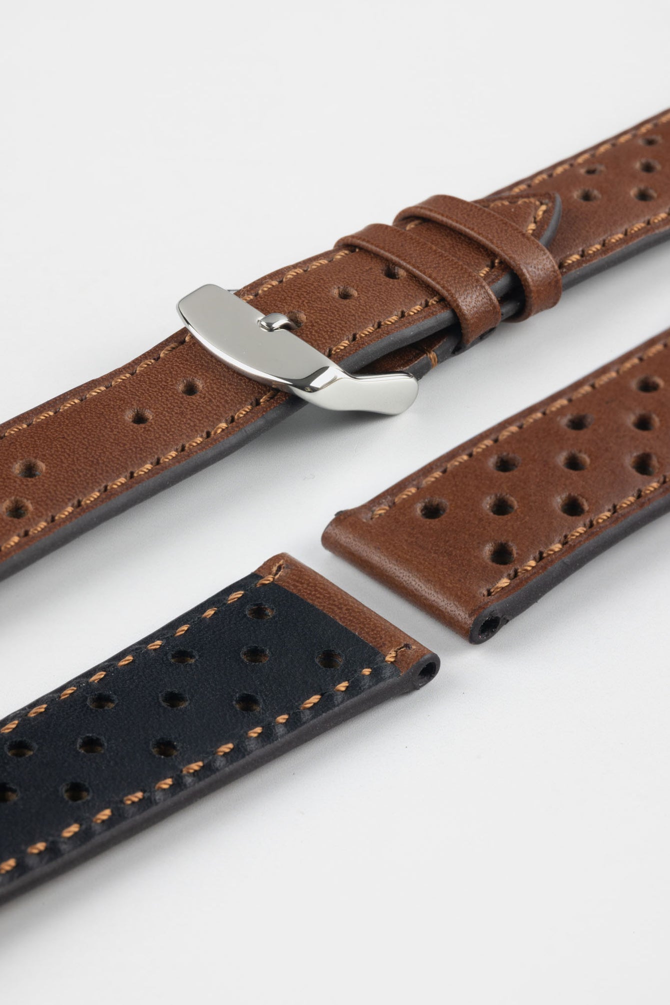 Close-up product shot of brown perforated leather watch strap components with contrast stitching, including one fitted with a polished silver deployment clasp. Additional strap sections, including one with a black underside, are arranged on a plain light background, highlighting the leather texture, perforations, and metal clasp details.