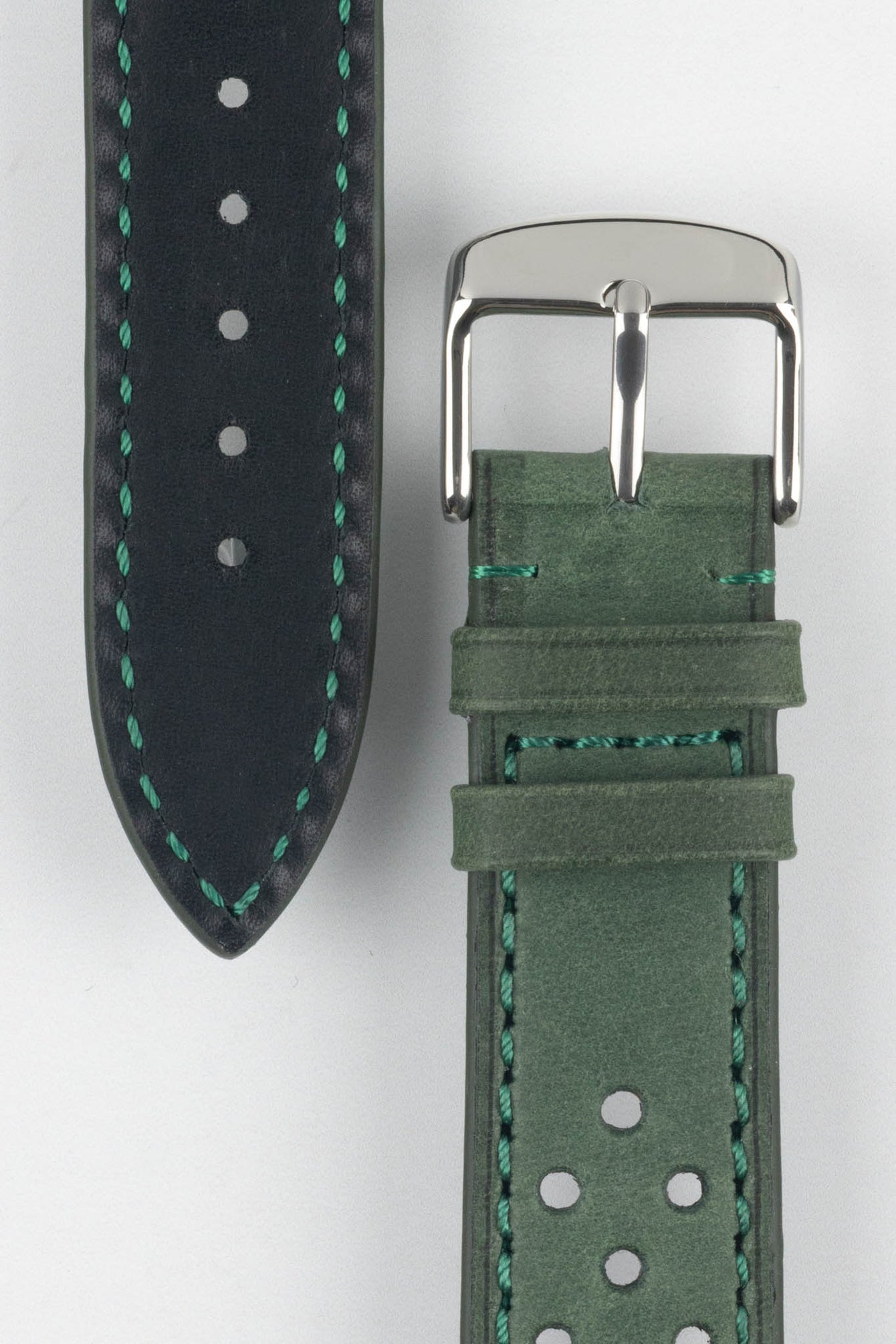 Close-up product shot of a green leather watch strap paired with a black underside strap segment, both featuring contrast green stitching. A polished silver pin buckle is attached to the green strap, and the components are arranged on a plain light background to highlight the leather texture, stitching, and perforation details.
