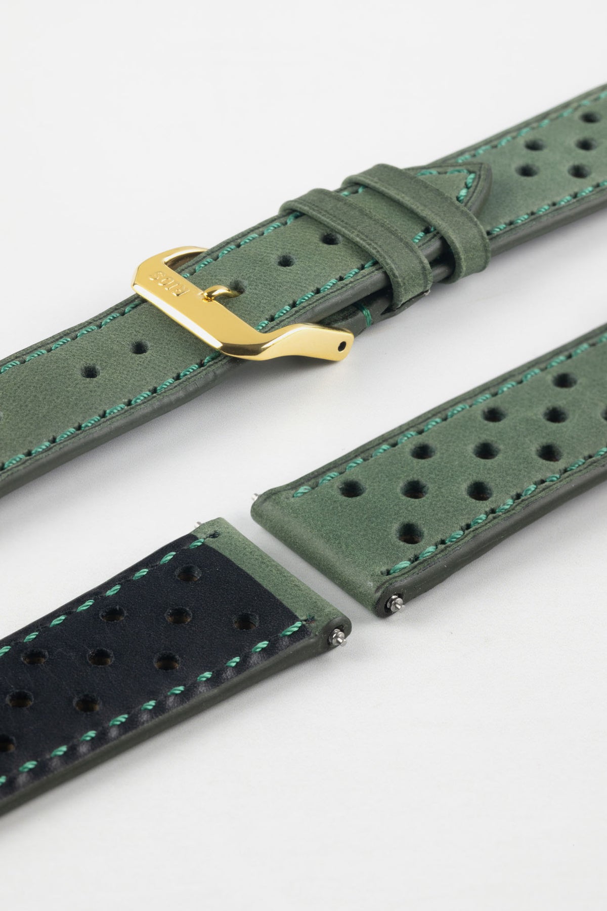 Close-up detail view of a forest green perforated leather rally watch strap displayed with one strap section detached, featuring a soft nubuck-style finish, turquoise contrast stitching, multiple motorsport-inspired perforations, dual keeper loops, a polished gold-tone RIOS buckle, quick-release spring bars, and a black leather lining. Displayed on a light grey background to highlight the premium handcrafted construction, contrasting underside, and vintage racing-inspired design.