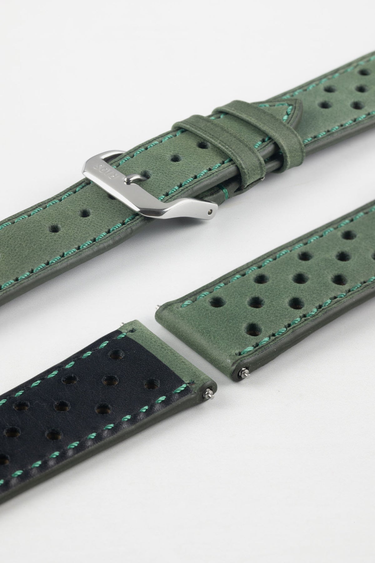 Close-up detail view of a forest green perforated leather rally watch strap displayed with one strap section detached, featuring a soft nubuck-style finish, turquoise contrast stitching, multiple motorsport-inspired perforations, dual keeper loops, a polished stainless steel RIOS buckle, quick-release spring bars, and a black leather lining. Displayed on a light grey background to highlight the premium handcrafted construction, contrasting underside, and vintage racing-inspired design.