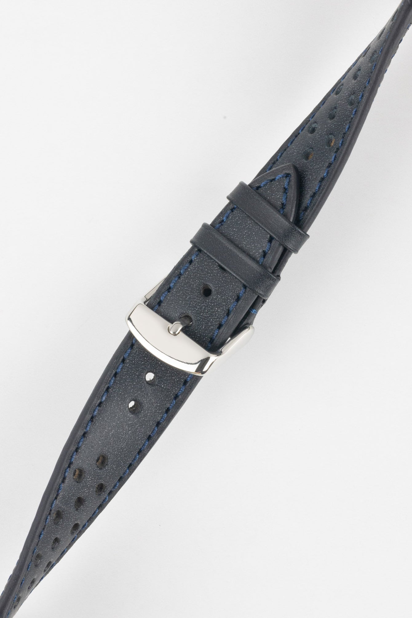 Close-up product shot of a grey-blue perforated leather watch strap with blue contrast stitching, fitted with a polished silver deployment clasp. The strap is laid diagonally on a plain light background, highlighting the textured leather surface, stitching detail, perforations, and metal clasp hardware.