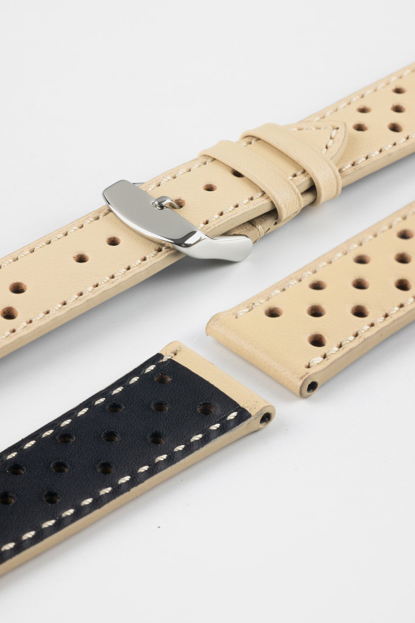 Close-up product shot of beige perforated leather watch strap components with contrasting stitching, including one fitted with a polished silver deployment clasp. Additional strap pieces, including one with a black underside, are arranged on a plain light background to highlight the perforations, texture, and metal hardware.