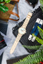 Vintage-style Studio Underd0g chronograph watch with a pastel green and cream dial, fitted with a sand-coloured perforated leather rally strap, displayed on a black equipment case alongside a multitool, camera lens, sunglasses, leather accessories, and greenery, highlighting the strap's motorsport-inspired design and premium handcrafted leather construction.
