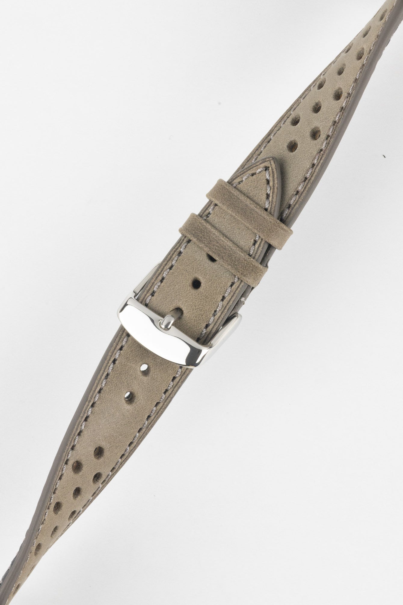 Close-up product shot of a grey suede leather watch strap with perforations and light contrast stitching, fitted with a polished silver pin buckle. The strap is laid at a slight diagonal on a plain light background, highlighting the soft texture, stitching detail, and buckle hardware.
