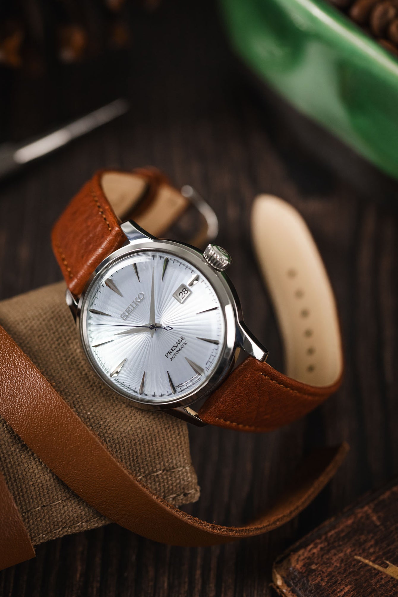 Curved watch strap by RIOS1931 fitted to a Seiko Presage watch leant against a Watch roll on wooden table