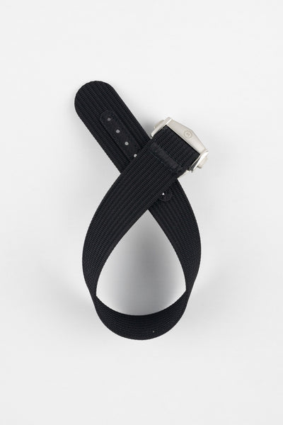 A top-down shot of a black ribbed-nylon watch strap coiled into a loop against a white background, featuring a brushed stainless steel buckle with a circular logo.