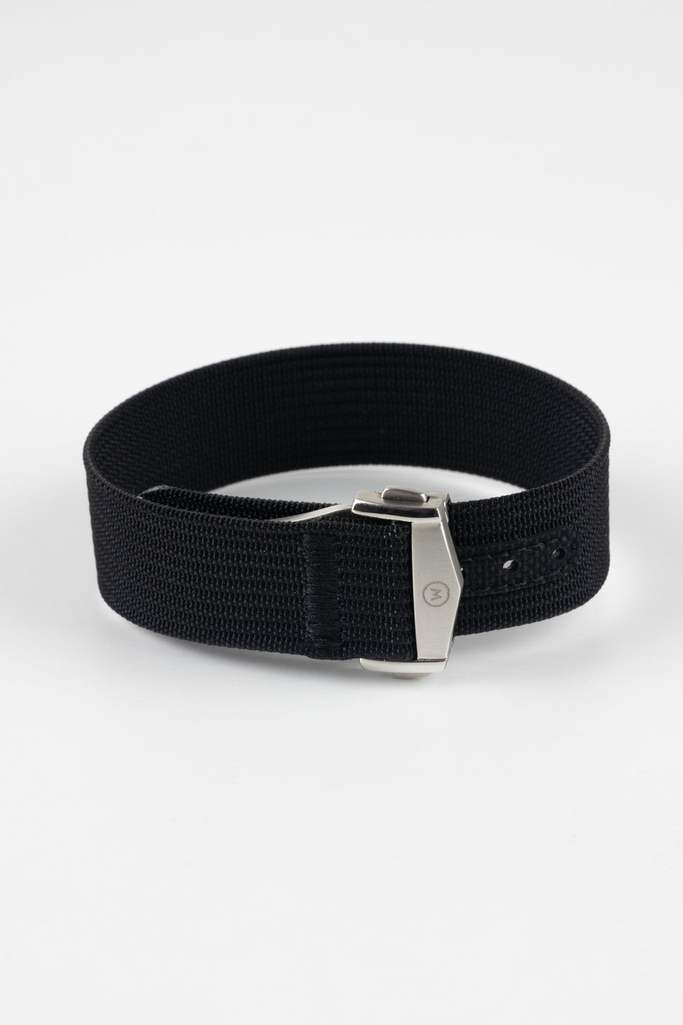 A three-quarter view of a black ribbed-nylon watch strap fastened into a loop, highlighting the brushed metal buckle and woven texture on a white background.