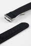 A close-up, angled shot of a black ribbed-nylon watch strap showing both the brushed stainless steel deployment buckle and the adjustment holes. The image highlights the fine woven texture of the fabric and the precision stitching near the metal clasp.