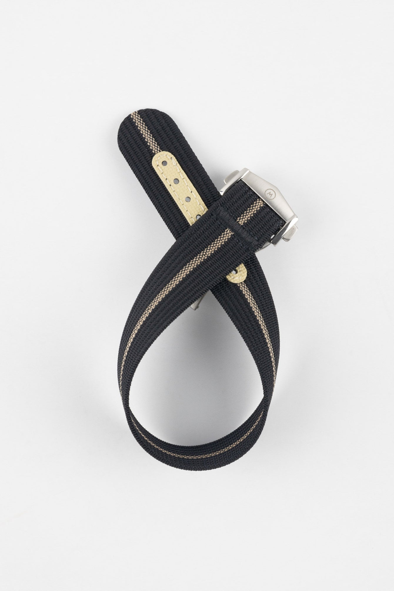 Black ribbed nylon watch strap with a central cream stripe, displayed looped and crossed on a light grey background. The strap features a brushed silver deployant clasp with an engraved logo and a cream-colored reinforced section with evenly spaced adjustment holes near the end.
