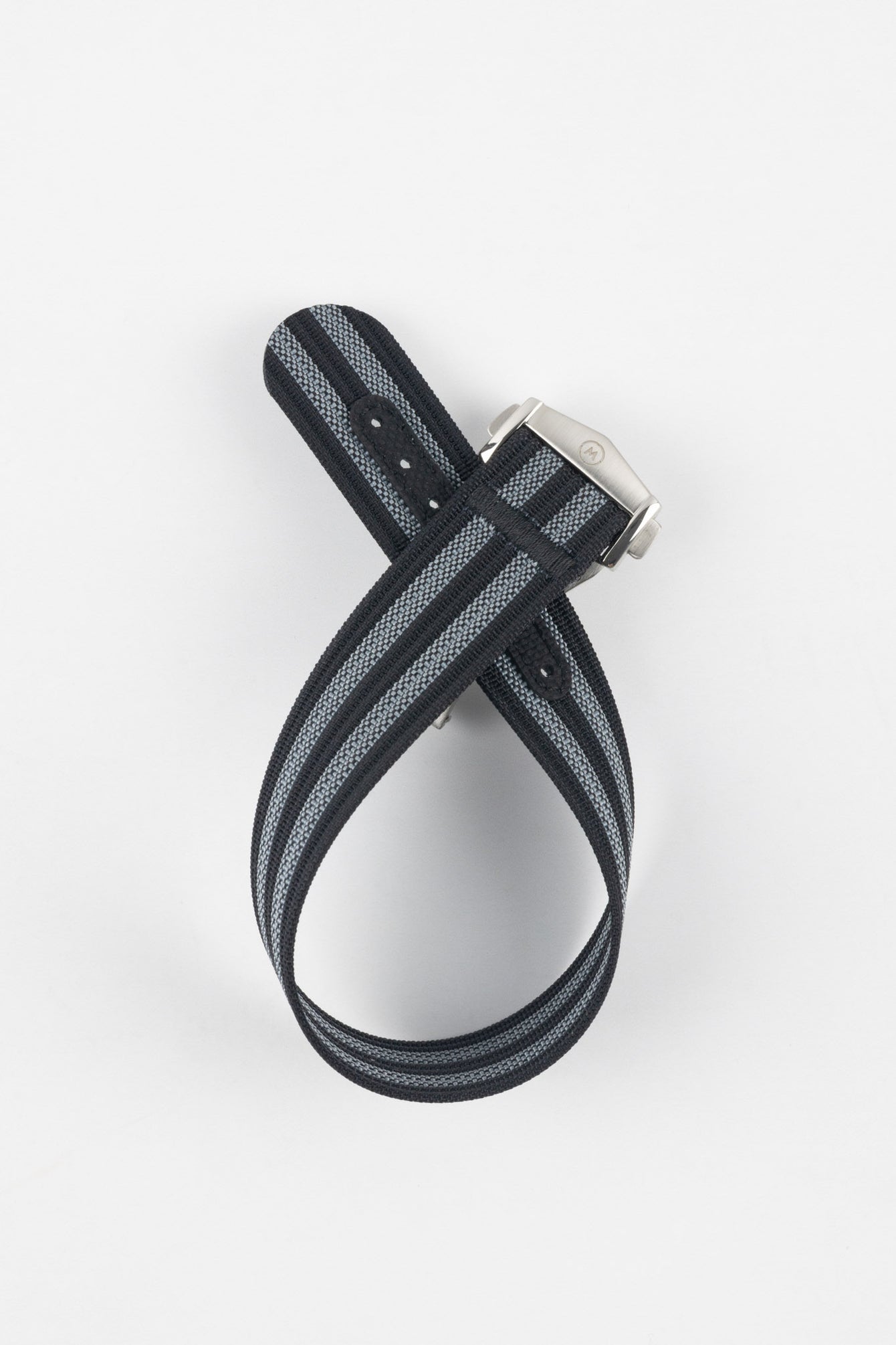 Black ribbed nylon watch strap with grey and white striped detailing, displayed looped and crossed on a light grey background. The strap features a brushed silver deployant clasp with an engraved logo and a dark reinforced section with adjustment holes near the end.