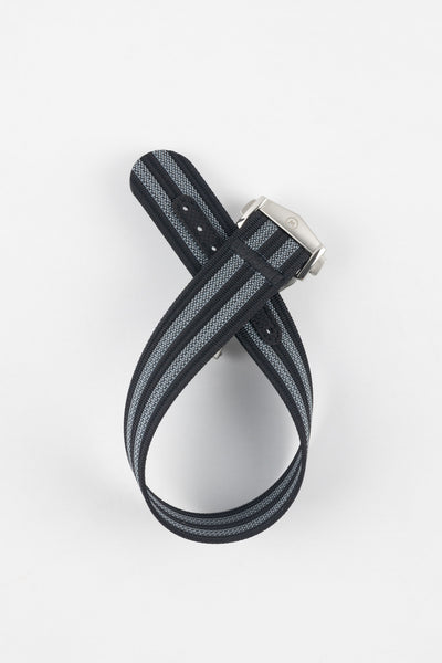 Black ribbed nylon watch strap with grey and white striped detailing, displayed looped and crossed on a light grey background. The strap features a brushed silver deployant clasp with an engraved logo and a dark reinforced section with adjustment holes near the end.