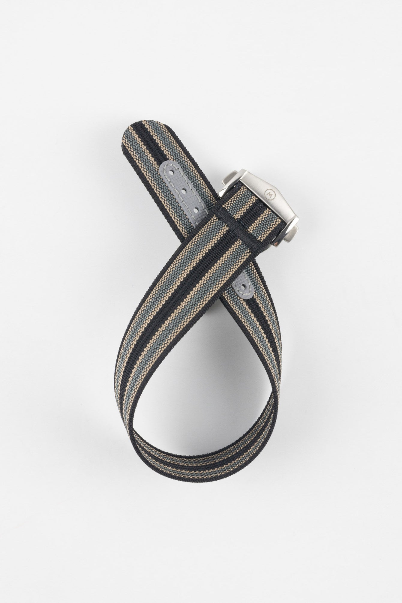 Striped ribbed nylon watch strap in black, grey, and cream tones, shown looped and crossed over itself on a light grey background, featuring a brushed silver deployant clasp with an engraved logo and visible adjustment holes along one section.