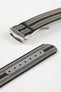 Angled close-up of a striped ribbed nylon watch strap in black, grey, and cream tones, featuring a brushed silver deployant clasp with an engraved logo, alongside a separate strap section with a grey reinforced panel and adjustment holes, all set against a light grey background.
