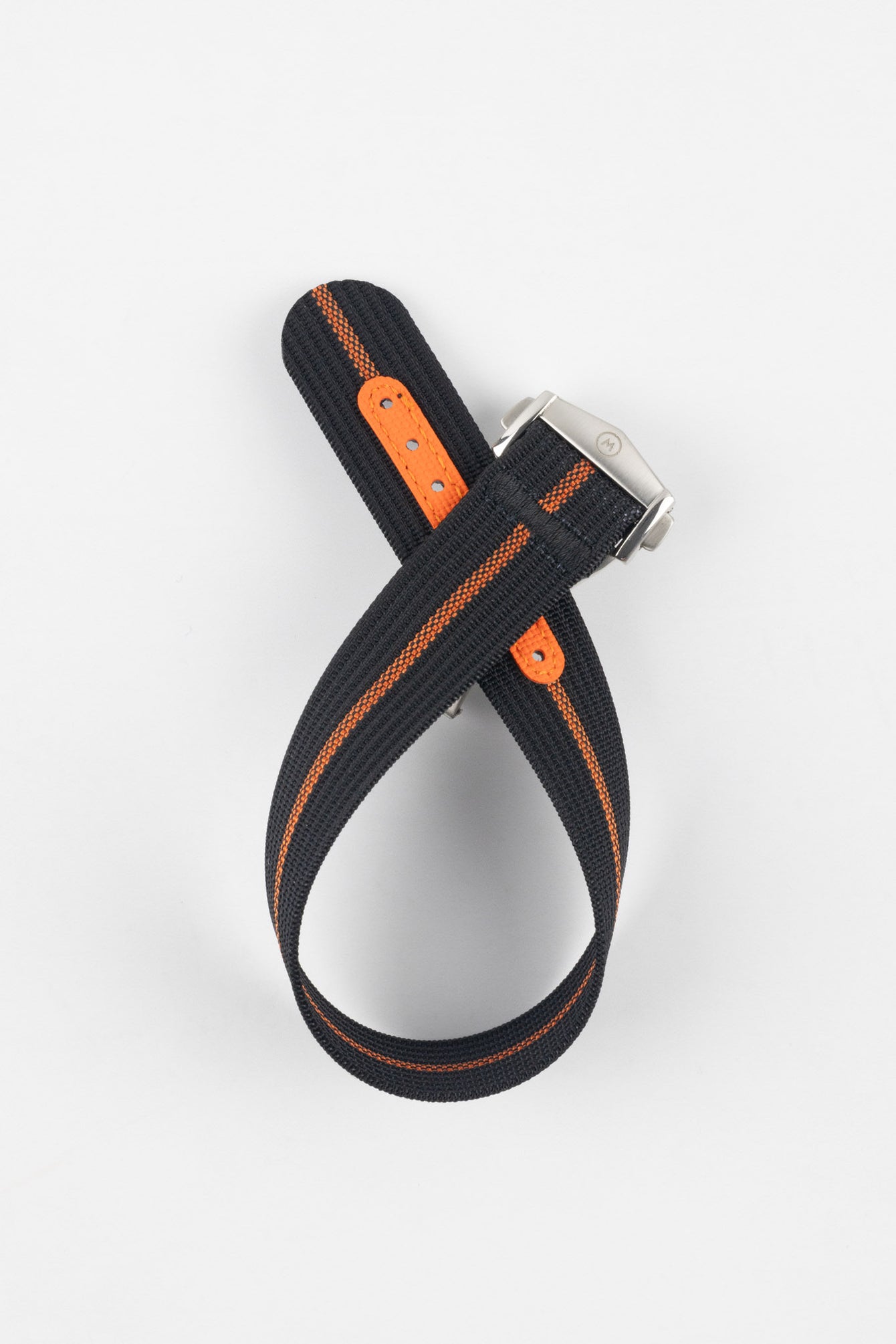 Striped ribbed nylon watch strap in black with a central orange stripe, displayed looped and crossed on a light grey background. The strap features a brushed silver deployant clasp with an engraved logo and a bright orange reinforced section with adjustment holes.