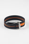 Close-up of a black ribbed nylon watch strap with a central orange stripe, arranged in a loop on a light grey background. The strap features a brushed silver deployant clasp with an engraved logo and a bright orange reinforced section with adjustment holes near the clasp.