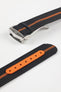 Angled close-up of a black ribbed nylon watch strap with a central orange stripe, featuring a brushed silver deployant clasp with an engraved logo. A separate section of the strap shows a bright orange reinforced panel with evenly spaced adjustment holes, all displayed on a light grey background.