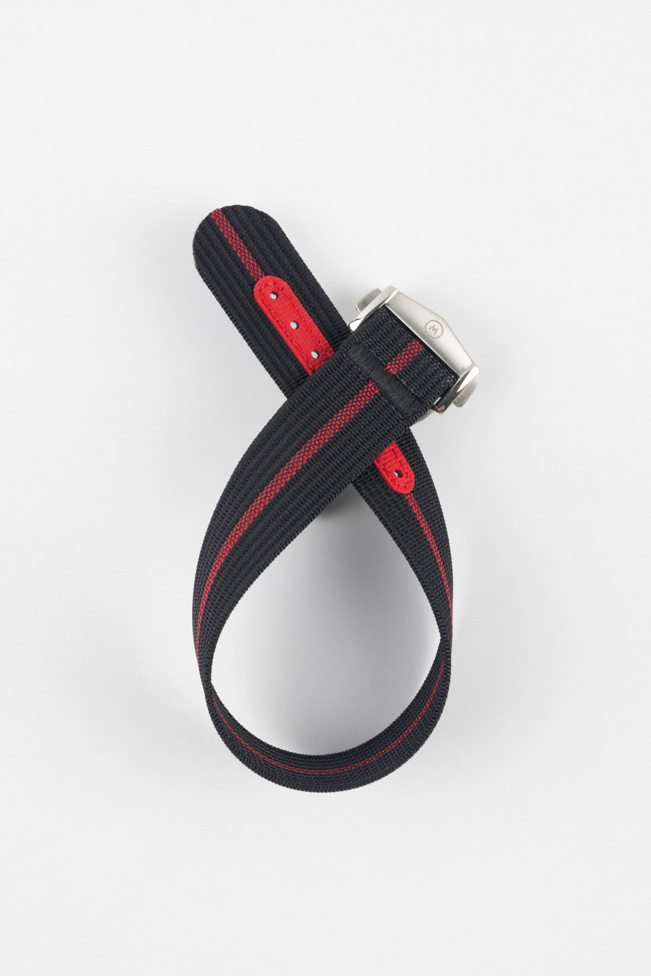 Black ribbed nylon watch strap with a central red stripe, displayed looped and crossed on a light grey background. The strap features a brushed silver deployant clasp with an engraved logo and a red reinforced section with adjustment holes along the underside.