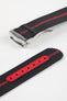 Angled close-up of a black ribbed nylon watch strap with a central red stripe, featuring a brushed silver deployant clasp with an engraved logo. A separate strap section displays a red reinforced panel with evenly spaced adjustment holes, all set against a light grey background.