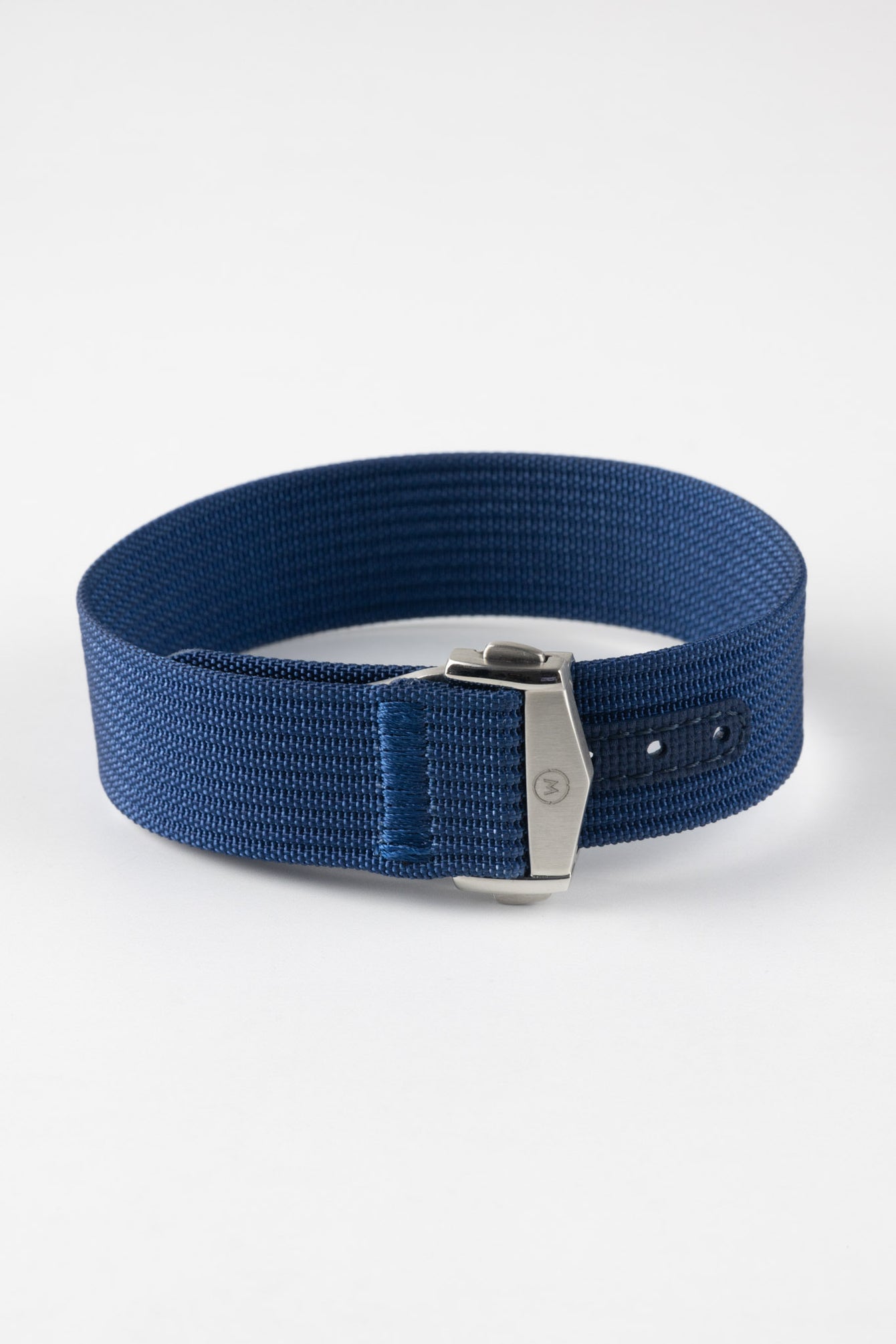 A three-quarter view of a blue ribbed-nylon watch strap fastened into a loop, highlighting the brushed metal buckle and woven texture on a white background.