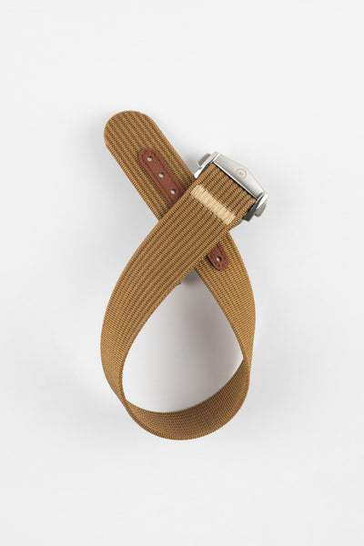 A top-down shot of a brown ribbed-nylon watch strap coiled into a loop against a white background, featuring a brushed stainless steel buckle with a circular logo.