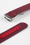 A three-quarter view of a burgundy ribbed-nylon watch strap fastened into a loop, highlighting the brushed metal buckle and woven texture on a white background.