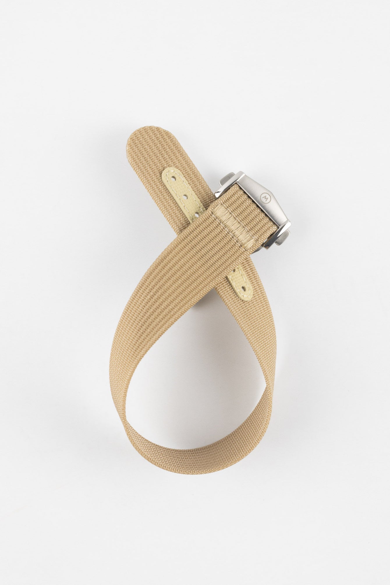 Light cream ribbed nylon watch strap displayed looped on a light grey background, featuring a brushed silver deployant clasp with an engraved logo. The strap includes a matching cream reinforced section with evenly spaced adjustment holes, highlighting its textured weave and clean, minimalist design.
