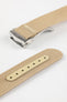Angled close-up of a light cream ribbed nylon watch strap showing the textured woven surface and a brushed silver deployant clasp with an engraved logo. A separate strap section displays a matching cream reinforced panel with neatly stitched edges and evenly spaced adjustment holes, all set against a clean light grey background.