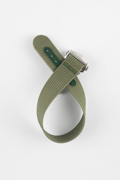 A top-down shot of a green ribbed-nylon watch strap coiled into a loop against a white background, featuring a brushed stainless steel buckle with a circular logo.