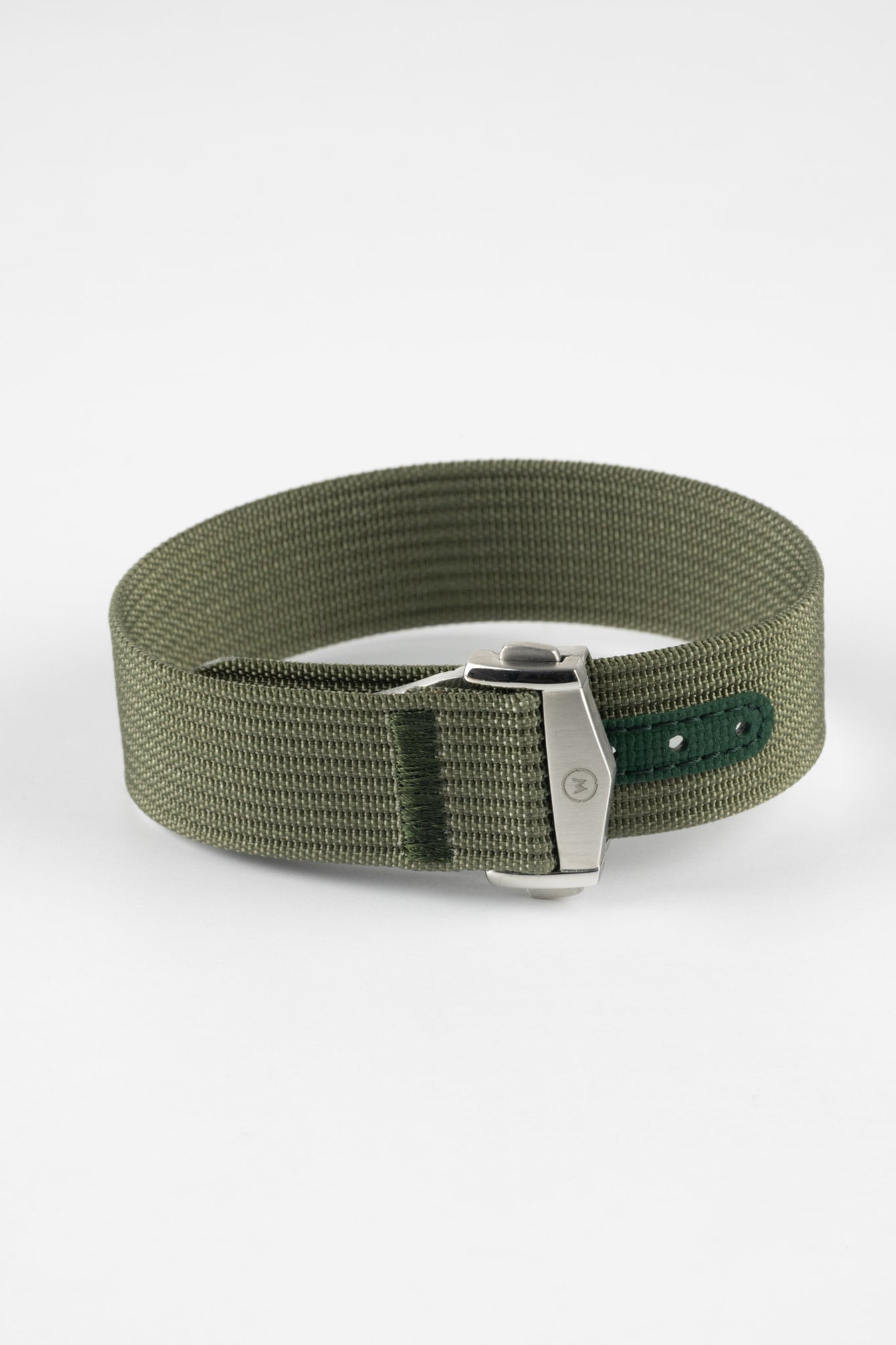 A three-quarter view of a green ribbed-nylon watch strap fastened into a loop, highlighting the brushed metal buckle and woven texture on a white background.