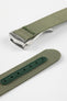 A close-up, angled shot of a green ribbed-nylon watch strap showing both the brushed stainless steel deployment buckle and the adjustment holes. The image highlights the fine woven texture of the fabric and the precision stitching near the metal clasp.