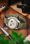 An Omega X Swatch MoonSwatch fitted to a green ribbed nylon military strap with a brushed steel deployment clasp in a lifestyle setting.