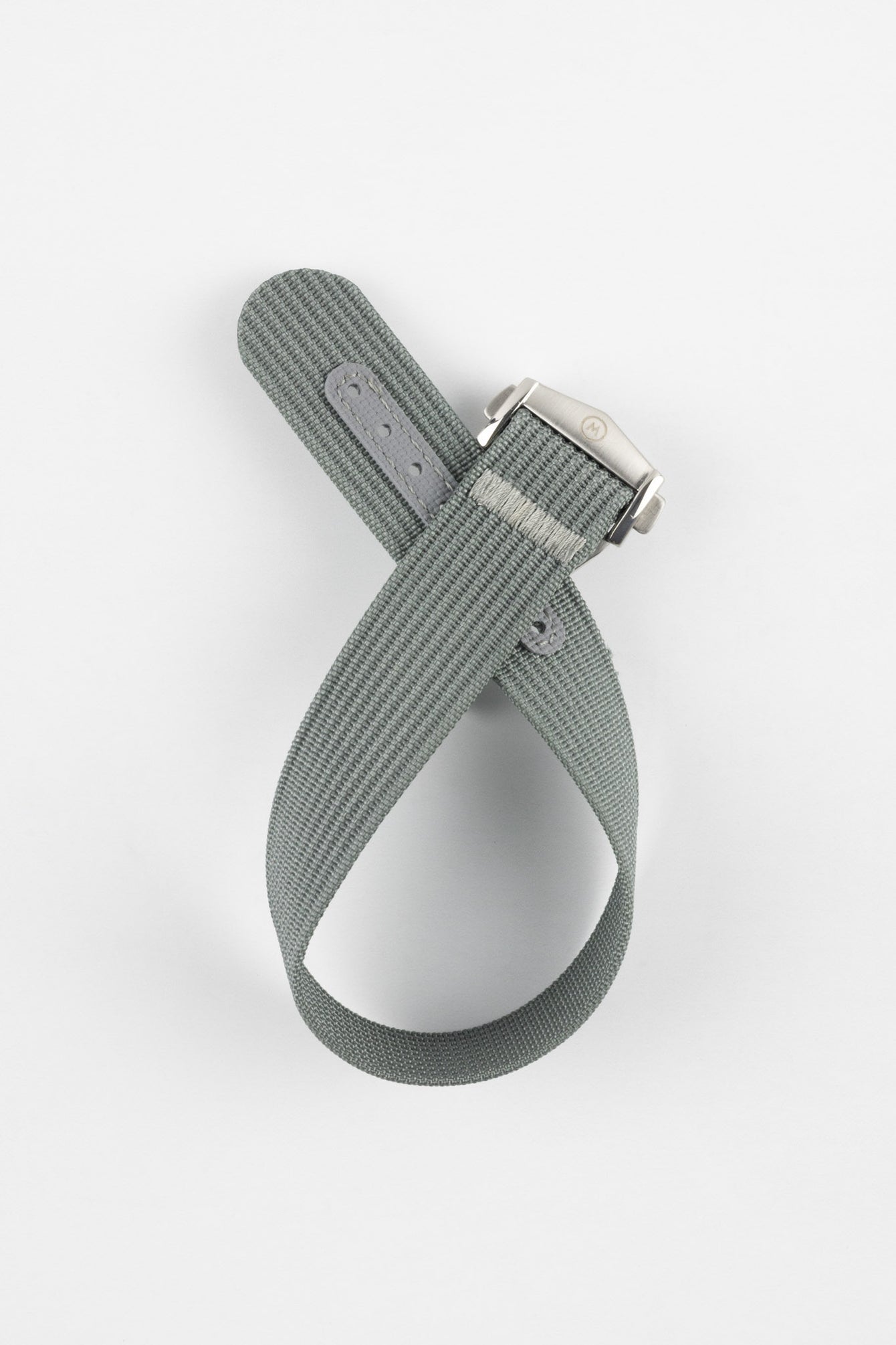 A top-down shot of a grey ribbed-nylon watch strap coiled into a loop against a white background, featuring a brushed stainless steel buckle with a circular logo.