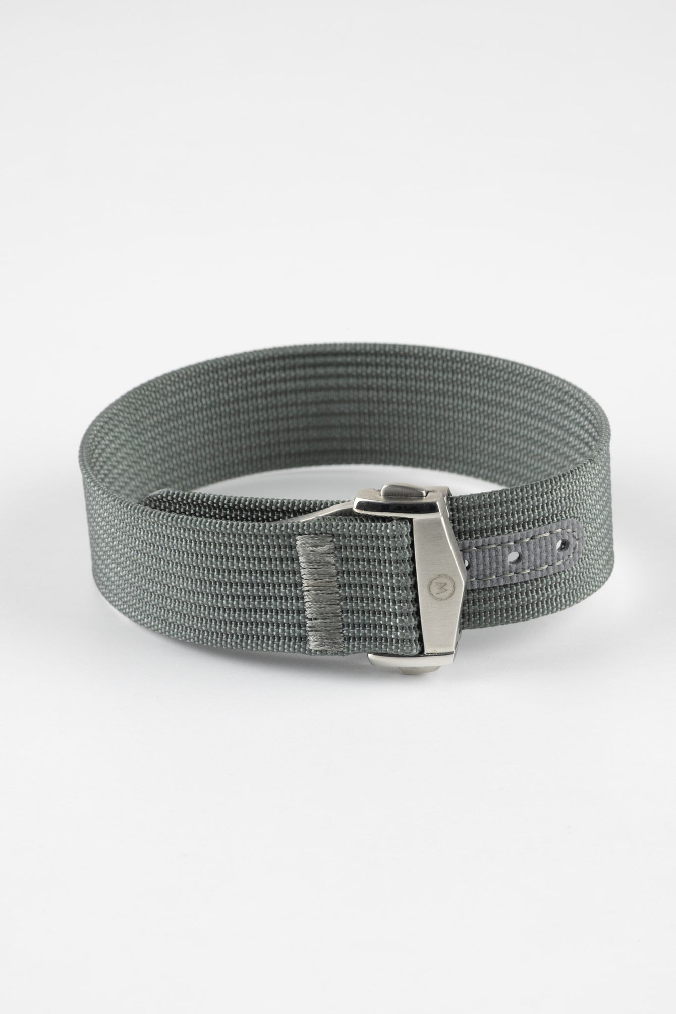 A three-quarter view of a grey ribbed-nylon watch strap fastened into a loop, highlighting the brushed metal buckle and woven texture on a white background.