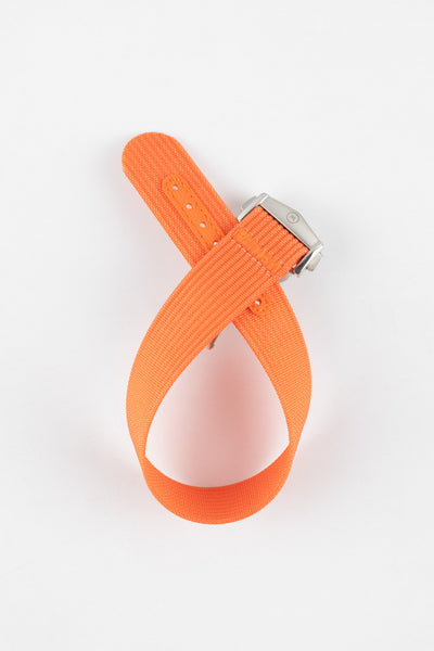 Bright orange ribbed nylon watch strap displayed looped on a light grey background, featuring a textured woven surface and a brushed silver deployant clasp with an engraved logo. The strap includes an orange reinforced section with evenly spaced adjustment holes, highlighting its bold color and durable construction.