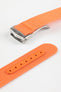 Angled close-up of a bright orange ribbed nylon watch strap highlighting the textured woven surface and a brushed silver deployant clasp with an engraved logo. A separate strap section shows an orange reinforced panel with neatly stitched edges and evenly spaced adjustment holes, all displayed against a clean light grey background.