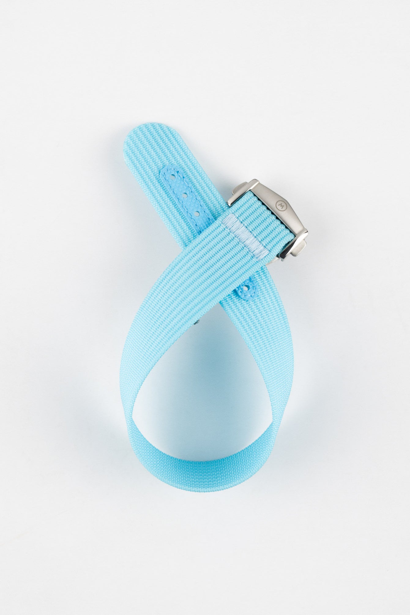 Light turquoise ribbed nylon watch strap displayed looped on a light grey background, featuring a finely textured woven surface and a brushed silver deployant clasp with an engraved logo. The strap includes a matching turquoise reinforced section with evenly spaced adjustment holes, emphasizing its fresh color and durable construction.