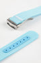 Angled close-up of a light turquoise ribbed nylon watch strap highlighting the fine woven texture and a brushed silver deployant clasp with an engraved logo. A separate strap section shows a matching turquoise reinforced panel with neatly stitched edges and evenly spaced adjustment holes, all displayed on a clean light grey background.