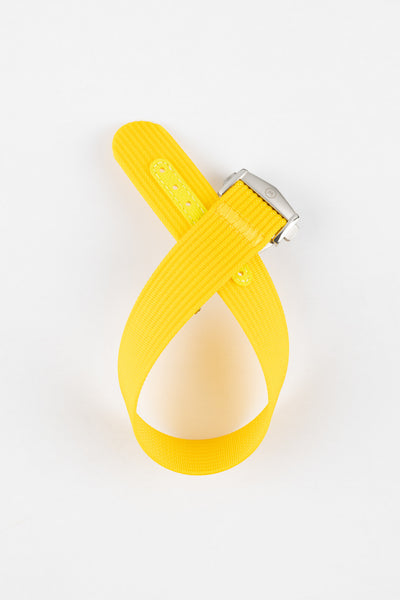 Bright yellow ribbed nylon watch strap displayed looped on a light grey background, featuring a textured woven surface and a brushed silver deployant clasp with an engraved logo. The strap includes a matching yellow reinforced section with evenly spaced adjustment holes, highlighting its vibrant color and durable construction.
