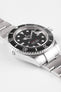 Angled close-up of a stainless steel Rolex Sea-Dweller watch showing the black dial, date magnifier, rotating bezel, and brushed metal bracelet against a plain background.