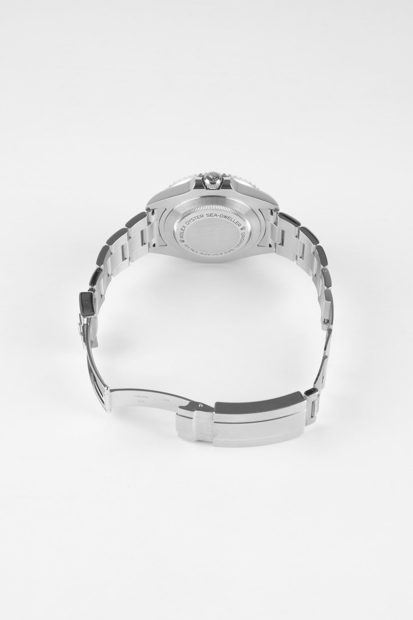 Back view of a stainless steel Rolex Sea-Dweller watch showing the engraved caseback and open metal bracelet against a white background.