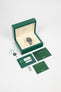 Rolex Sea-Dweller watch displayed in an open green presentation box with warranty card, manuals, spare links, and tags arranged on a white background.