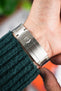 Close-up of a stainless steel Rolex watch clasp with engraved crown logo, worn on a wrist next to a green knit sleeve.