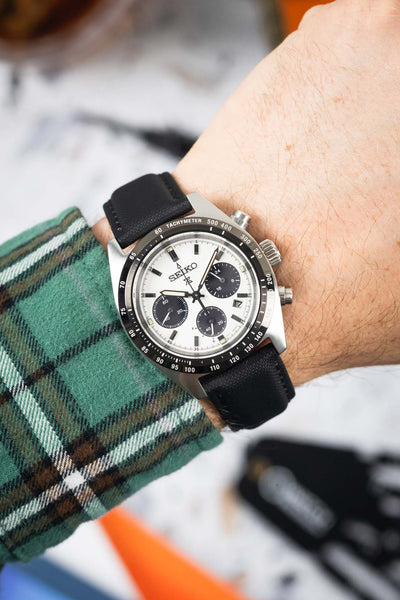 Close-up of a Seiko chronograph with a white dial on a black strap worn on a wrist.