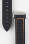 Close-up of a black textured watch strap with orange contrast stitching, showing one section with evenly spaced adjustment holes and the other attached to a brushed silver deployant clasp with an engraved logo, set against a light grey background.