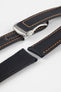 Angled close-up of a black textured watch strap with orange contrast stitching, featuring a brushed silver deployant clasp with an engraved logo, alongside separate strap sections, all displayed on a light grey background.