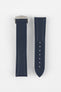 Two dark blue textured watch strap pieces displayed vertically on a light grey background, featuring subtle matching blue stitching; one strap is fitted with a brushed silver deployant clasp, while the other shows a row of adjustment holes down the center.