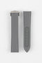 Two grey textured watch strap pieces displayed vertically on a light grey background, featuring subtle light grey stitching; one strap is fitted with a brushed silver deployant clasp with an engraved logo, while the other shows a row of evenly spaced adjustment holes down the center.