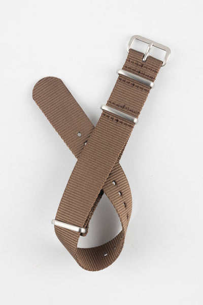 Close-up product shot of a brown ribbed nylon NATO-style watch strap with brushed metal buckle and keepers, laid against a plain light background, highlighting its woven texture and adjustment holes.